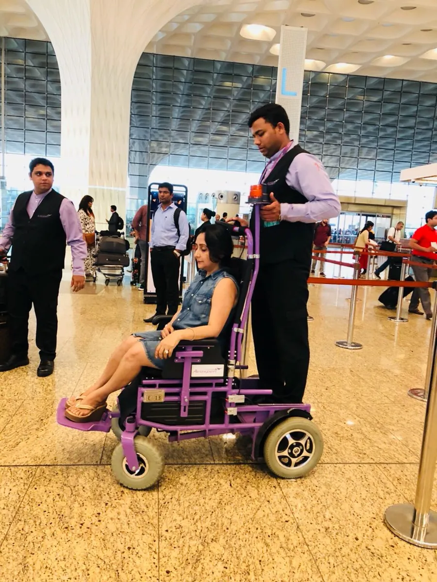 Airport attendant guiding a passenger in a wheelchair towards the departure gates
